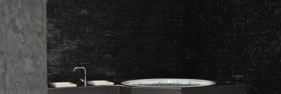Badezimmer mit runder Wanne vor einer dunklen Natursteinwand